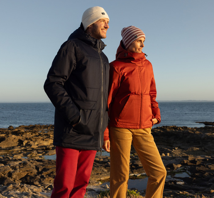 A man and a woman at the seaside wearing Mousqueton parkas and hats
